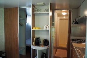 A compact kitchenette with a stove, coffee maker, and shelves with kitchenware. - Tuscan Mobile home with Covered Porch (Capannole)