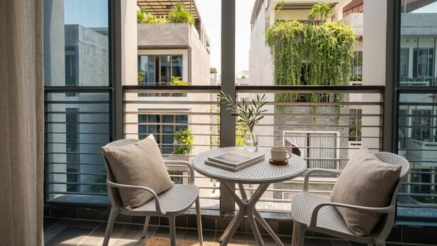 A balcony with two chairs, a small table, and a view of buildings with greenery. - THE GRACE An Thuong Hotel & Apartment (Da Nang)