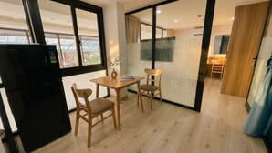 A modern kitchen with a black refrigerator, wooden chairs, a small table, and a view through a glass door. - THE GRACE An Thuong Hotel & Apartment (Da Nang)