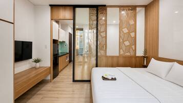 A modern hotel room with a bed, a TV, a wooden desk, and a sliding door leading to a bathroom.