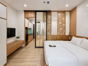 Habitación de hotel moderna con cama, televisor, escritorio de madera y puerta corredera hacia un baño.