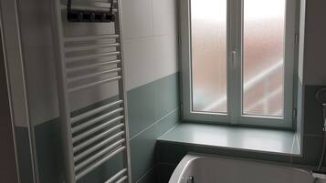 A bathroom with a bathtub, a window, and a towel rack.