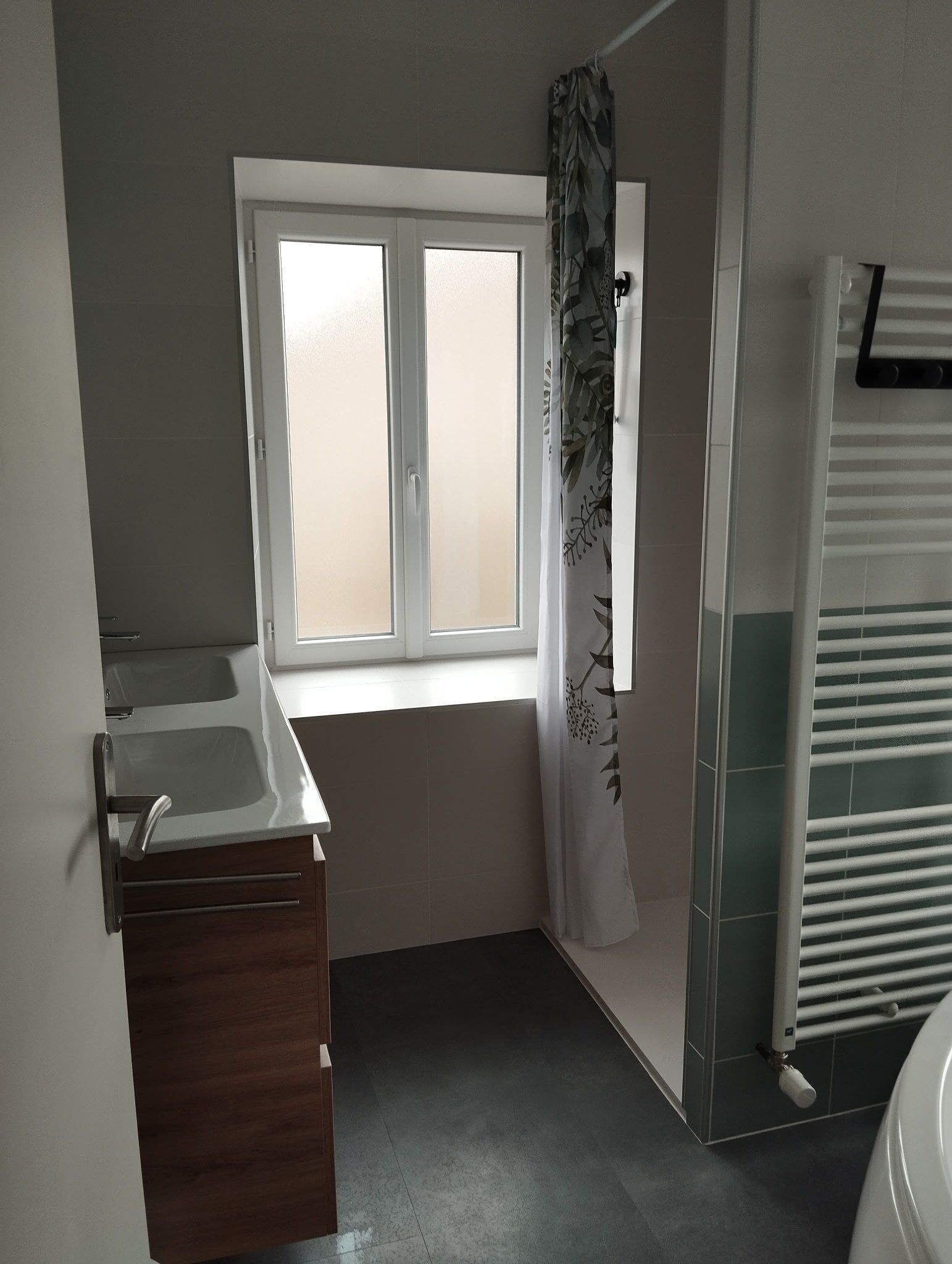 Et badeværelse med et vindue, bruser, vask og toilet.