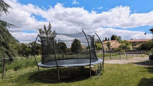 A trampoline with a safety net in a grassy yard with trees and a house in the background. - La Canissa Carrada family canopy room (Chaspuzac)