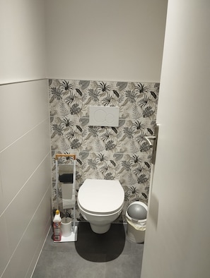 Un baño con inodoro, lavamanos, espejo y un portalápices para escobilla.