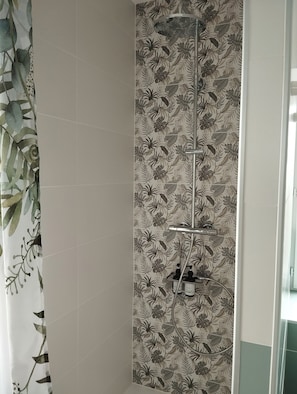 Ducha con cabezal de ducha de lluvia vertical, cabezal de ducha manual y panel de control en la pared.