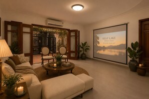 Un salon chaleureux avec un canapé, des fauteuils, une table basse et un grand écran diffusant une œuvre d’art représentant un paysage.