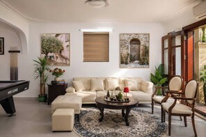 A living room with a pool table, a sofa, a coffee table, and a chair. There are two paintings on the wall, a potted plant, and a window with a view of the outside. - 500m2 Jacuzzi House 6BR West Lake/Billiard/BBQ (Hà Nội)