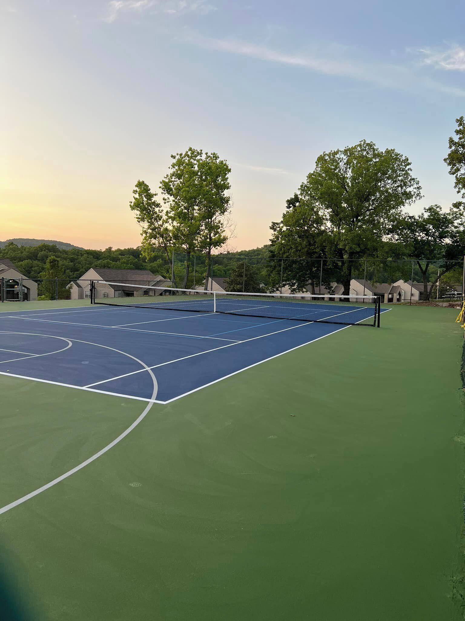 A tennis court with a net, surrounded by trees and buildings.