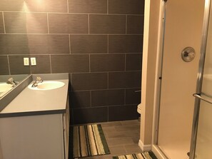 A bathroom with dark tiles, a white sink, a mirror, and a shower area. - Situated on a small gated community just a 12 minute from all Disney parks (Davenport)