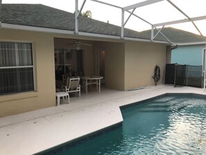 Ein Schwimmbecken mit überdachter Terrasse, einem Deckenventilator und einem Tisch mit Stühlen.