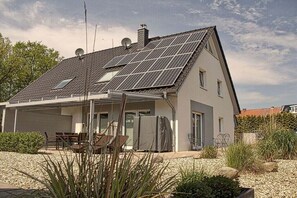 Una casa moderna con techo inclinado, paneles solares, un porche cubierto y un camino de entrada de grava.
