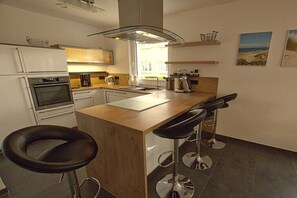 Una cocina moderna con una isla central, taburetes de bar y vistas al exterior.