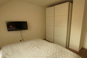 Un dormitorio con cama, televisor montado en la pared y armario.