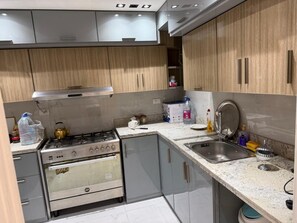 A kitchen with a gas stove, oven, sink, and wooden cabinets. - Spacious Family Apartment in Giza Near Pyramids (Giza Governorate)