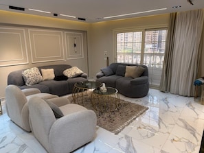 A modern living room with two sofas, a coffee table, and a large window with curtains. - Spacious Family Apartment in Giza Near Pyramids (Giza Governorate)
