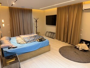 A modern bedroom with a bed, a flat-screen TV, a coat rack, and a radiator. - Spacious Family Apartment in Giza Near Pyramids (Giza Governorate)