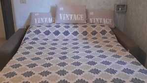 Een slaapkamer met een bedovertrek met een patroon, twee kussens met de tekst 'VINTAGE' en twee wanddecoraties met vlinderthema.