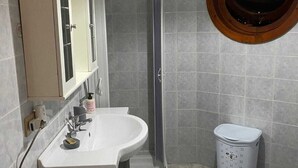Een badkamer met een douche, twee wasbakken, een toilet en een prullenbak.