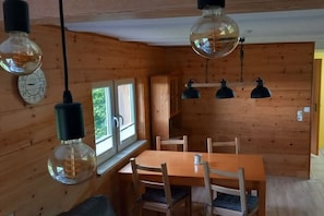 A wooden interior with a dining table, chairs, hanging light fixtures, and a window. - Holiday home with 2 bedrooms (Kurort Oybin OT Lückendorf)