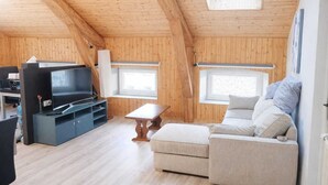 Una habitación con paneles de madera, un sofá, televisor y una pequeña mesa.