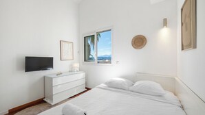 Une chambre à coucher comprenant un lit, un téléviseur, une commode, une fenêtre avec vue et un luminaire fixé au mur.