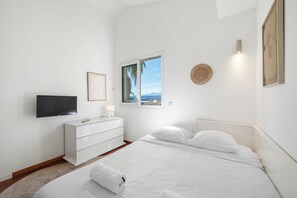 Ein Schlafzimmer mit Bett, Fernseher, Kommode, Fenster mit Blick und Wandlampe.