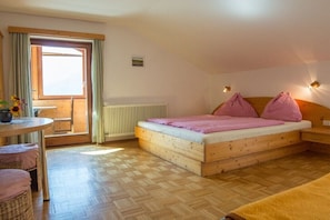 Un dormitorio con una cama de madera, una mesita pequeña, una silla y vistas al exterior a través de una puerta.