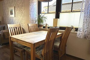 A dining area with a wooden table and chairs, a potted plant, and a window with blinds. - Holiday home in Lübbenau with swimming pool (Lübbenau)