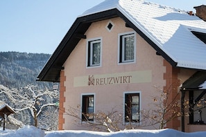 Ein Gebäude mit der Aufschrift 'REUZWIRT' auf der Fassade, umgeben von schneebedeckten Bäumen und einer Berglandschaft.