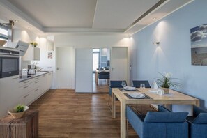 Eine moderne Küche mit integrierten Geräten, ein Essbereich mit einem Holztisch und blauen Stühlen sowie ein Gang zum Badezimmer.