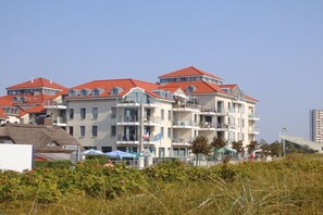 Ein mehrstöckiges Hotel mit Balkonen, wolkenlosem Himmel und einem Strand im Vordergrund.