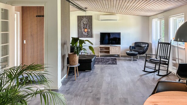 A modern living room with a TV, black leather chairs, a wooden dining table, and a large plant. - Beautiful home in Holbæk with WiFi (Holbæk)