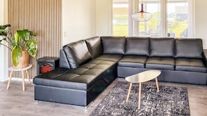 A modern living room with a sectional sofa, a small side table, a floor lamp, and a large potted plant. - Beautiful home in Holbæk with WiFi (Holbæk)