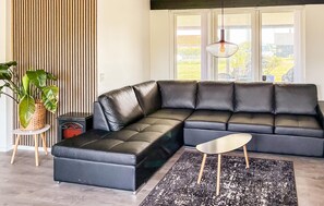 Ein modernes Wohnzimmer mit einem Ecksofa, einem kleinen Beistelltisch, einer Stehlampe und einer großen Topfpflanze.