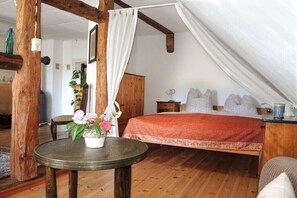 Ein Schlafzimmer mit Holzboden, einem Bett mit roter Decke, einem Nachttisch, einem Sessel und einem Tisch mit Topfpflanze.