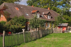 Ein traditionelles Backsteinhaus mit geneigtem Dach, einem Holzzaun und einer kleinen roten Struktur zur Rechten.