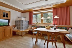 Ein gemütlicher Essbereich mit Holztisch, Stühlen, einer Bank, einem Fernseher und einem Fenster mit Vorhängen.