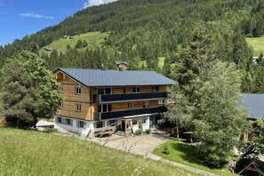 A multi-story wooden house with a sloped roof, surrounded by trees and a hilly landscape. - Holiday apartment in Hirschegg with balcony (Hirschegg)