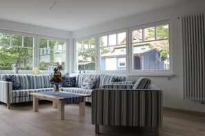 Ein Zimmer mit großem Fenster, einer Couch, einem Sessel und einem Tisch.