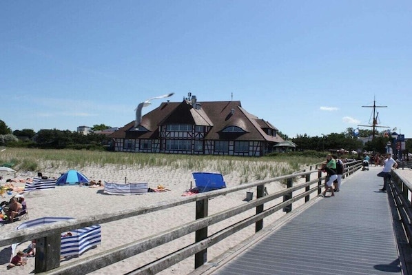 Eine Holzkonstruktion direkt am Strand mit geneigtem Dach, einem Holzsteg und Strandliegen.