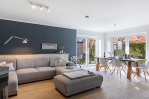 Ein modernes Wohnzimmer mit Sofa, Hocker und Essbereich mit Stühlen und Tisch.