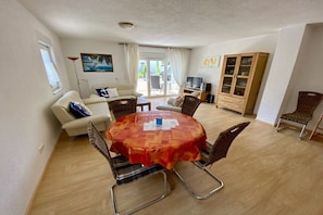Ein Essbereich mit einem runden Tisch, Stühlen, einer Couch, einem Schrank und einem Fernseher.