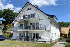 Ein zweistöckiges Gebäude mit Balkonen, ein Auto davor und ein klarer Himmel.