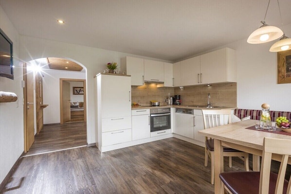 A modern kitchen with white cabinets, a wooden floor, and a dining area with a table and chairs. - Spitaler holiday apartment (Hippach)