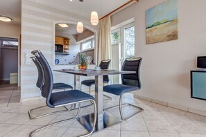 Ein Essbereich mit Tisch und Stühlen, eine Küche im Hintergrund und ein Gemälde an der Wand.