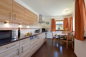 Eine moderne Küche mit Holzschränken, ein Essbereich mit Tisch und Stühlen sowie ein Fenster mit Vorhängen.