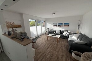 A modern living room with a sofa, coffee table, and a desk with a lamp. - Beach house connected to the sea (Kellenhusen)