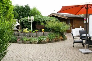 A patio area with a table and chairs, surrounded by potted plants and a wooden fence. - Holiday apartment with 2 bedrooms (21706 Drochtersen, Deutschland)