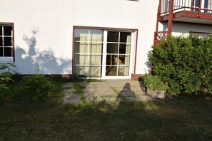 Ein Gebäude mit einer großen Schiebeglastür, einem kleinen Gartenbereich mit Blumentöpfen und einem sichtbaren Balkon.